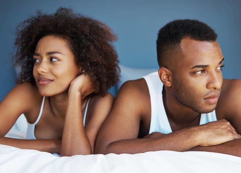 Man and woman sit in bed looking uncomfortably away from eachother