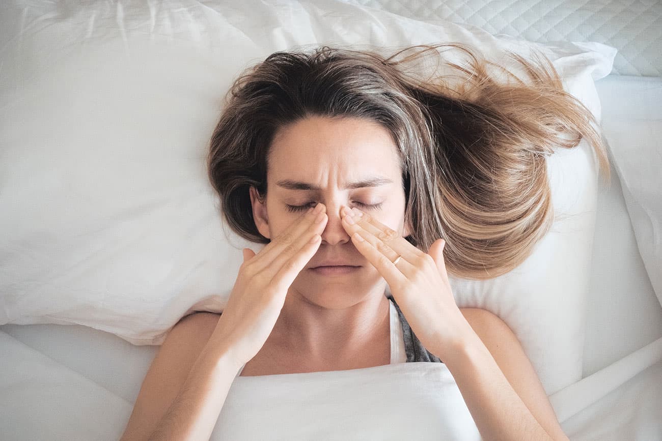 Woman lying in bed, rubbing her blocked sinuses caused by allergies