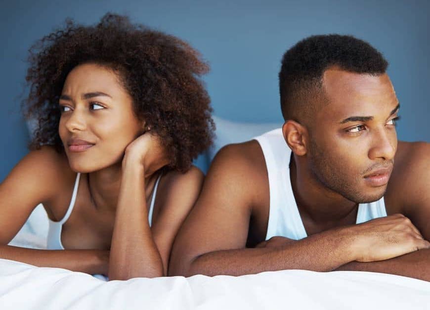 Man and woman sit in bed looking uncomfortable