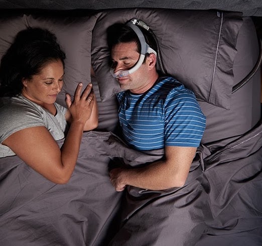 homme dort paisiblement avec son CPAP et sa femme contente dort aussi à côté
