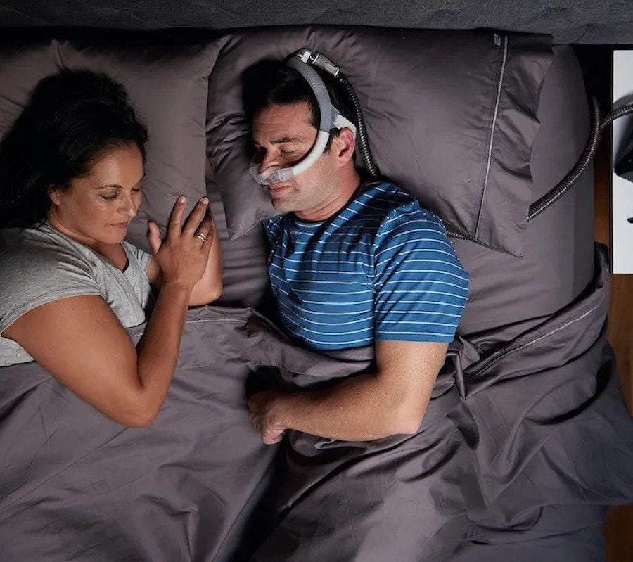Man sleeping comfortably in bed, wearing a CPAP nasal pillow mask