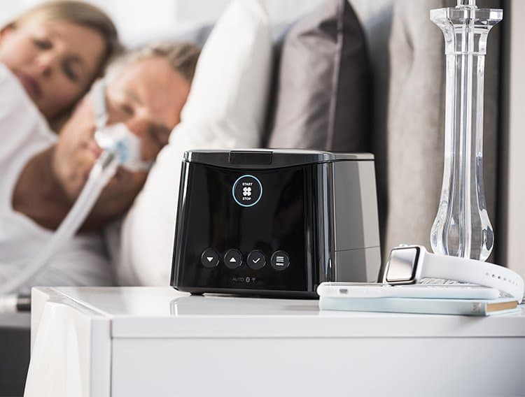 sleepstyle CPAP machine on a bedside table with a couple sleeping in the background