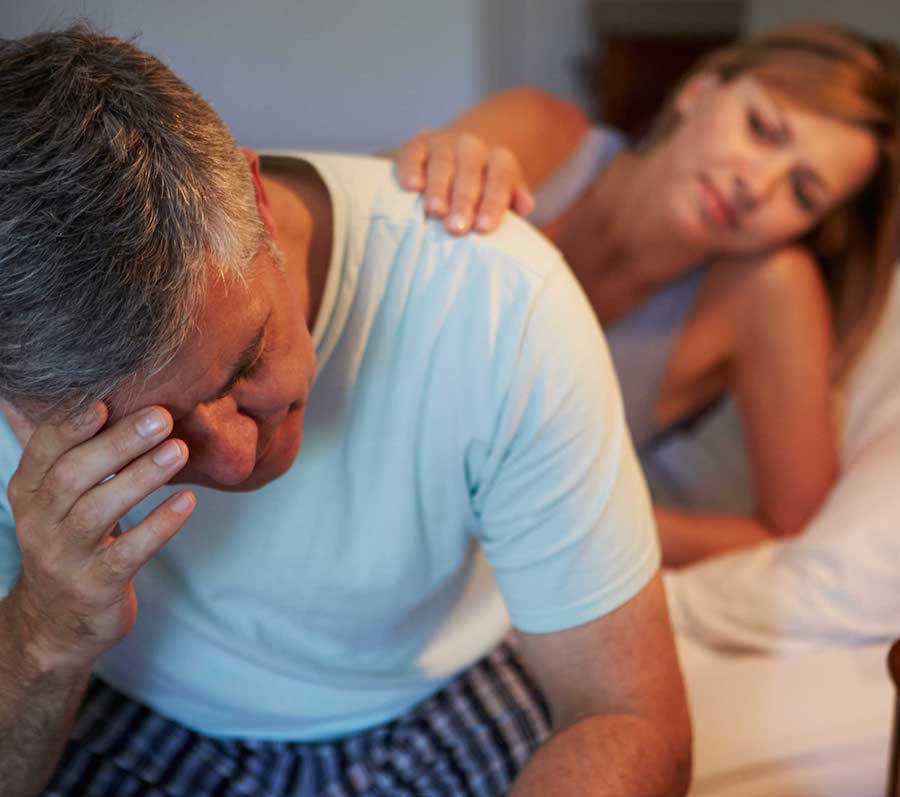 homme fatigué assis sur son lit avec sa femme inquiète