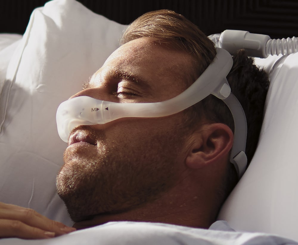 Man asleep in bed, wearing a Dreamwear nasal mask