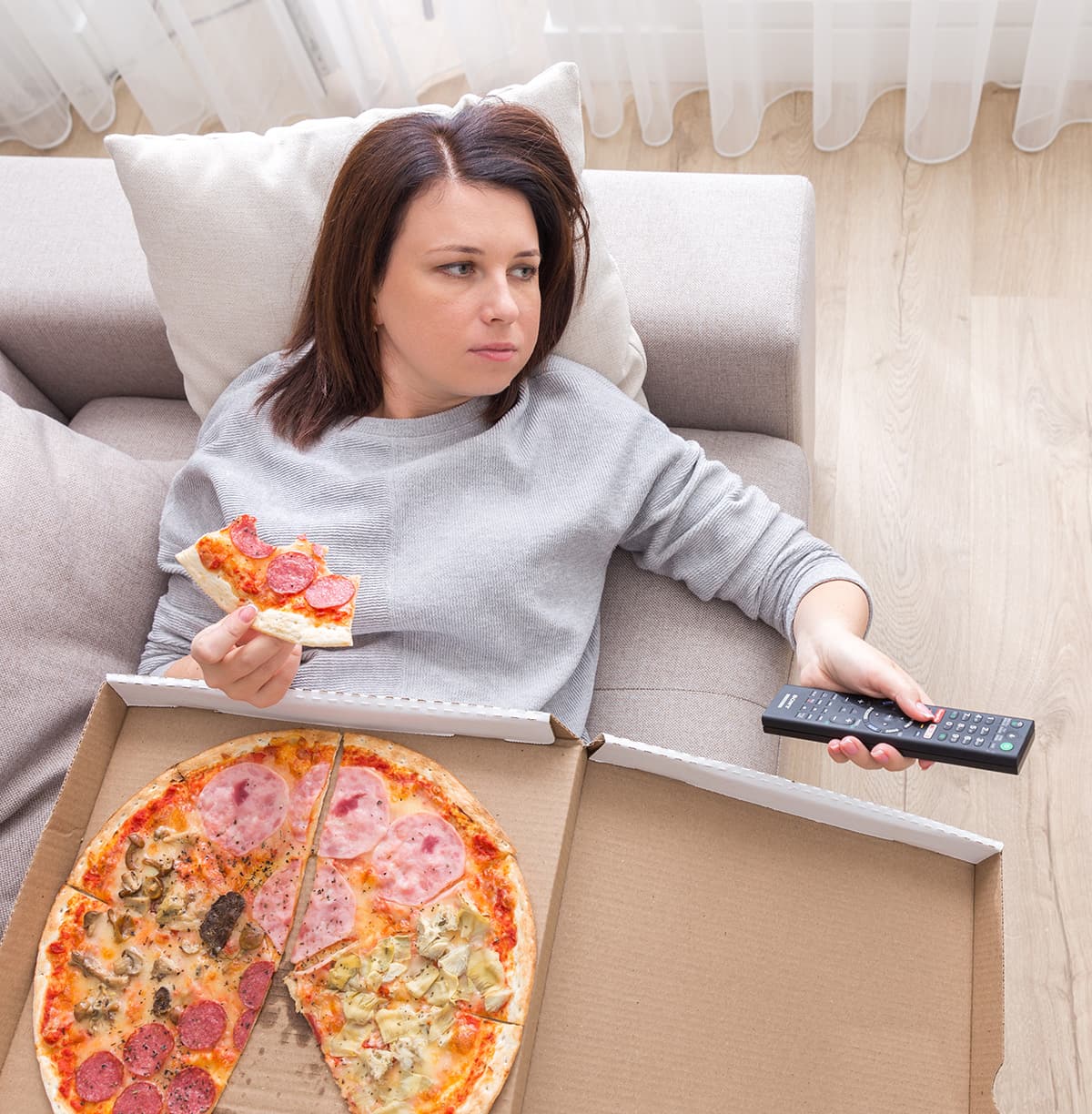 tired woman eating pizza on couch